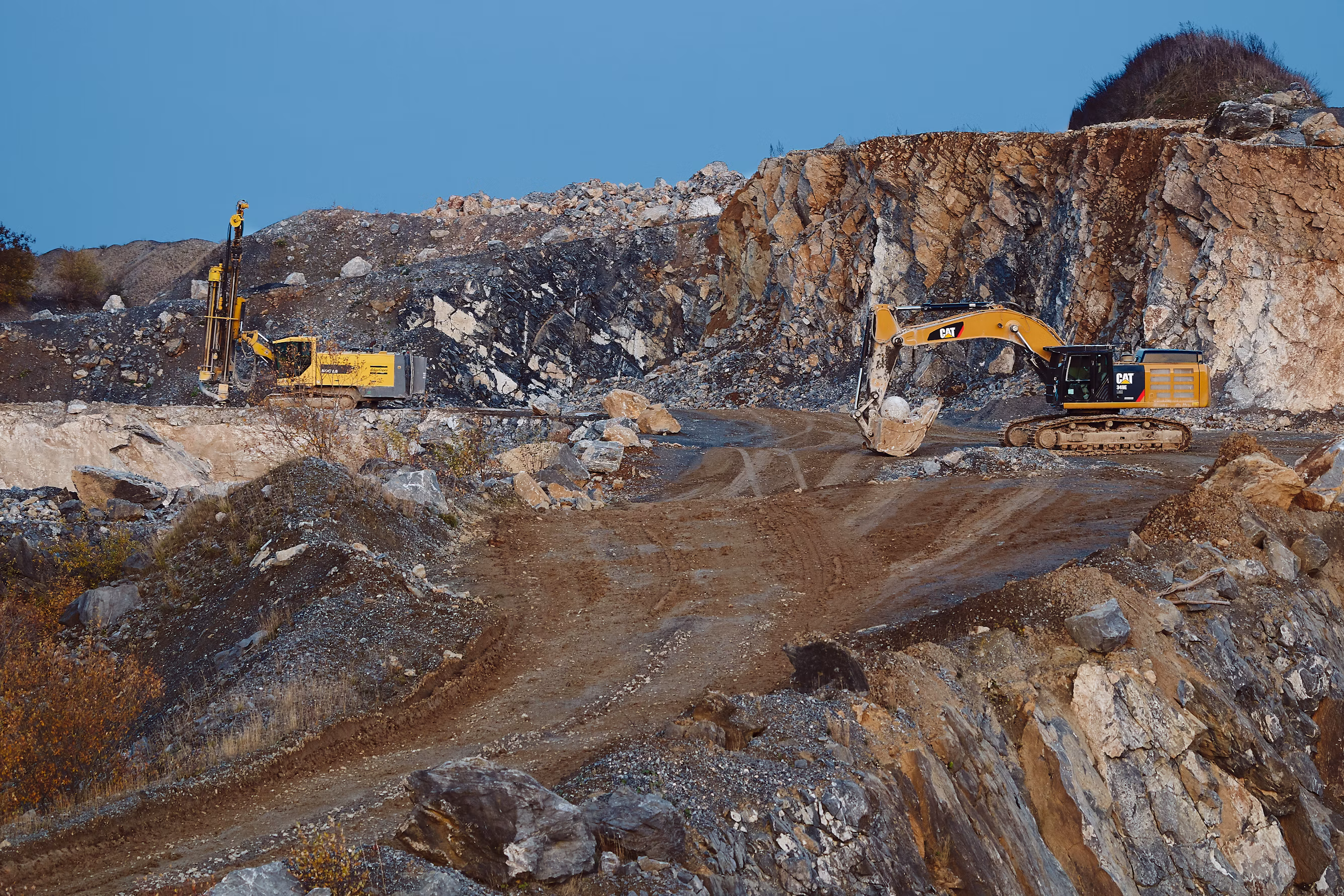 Heavy hydraulic excavators and drilling rigs excavating high-purity limestone at open quarry bench